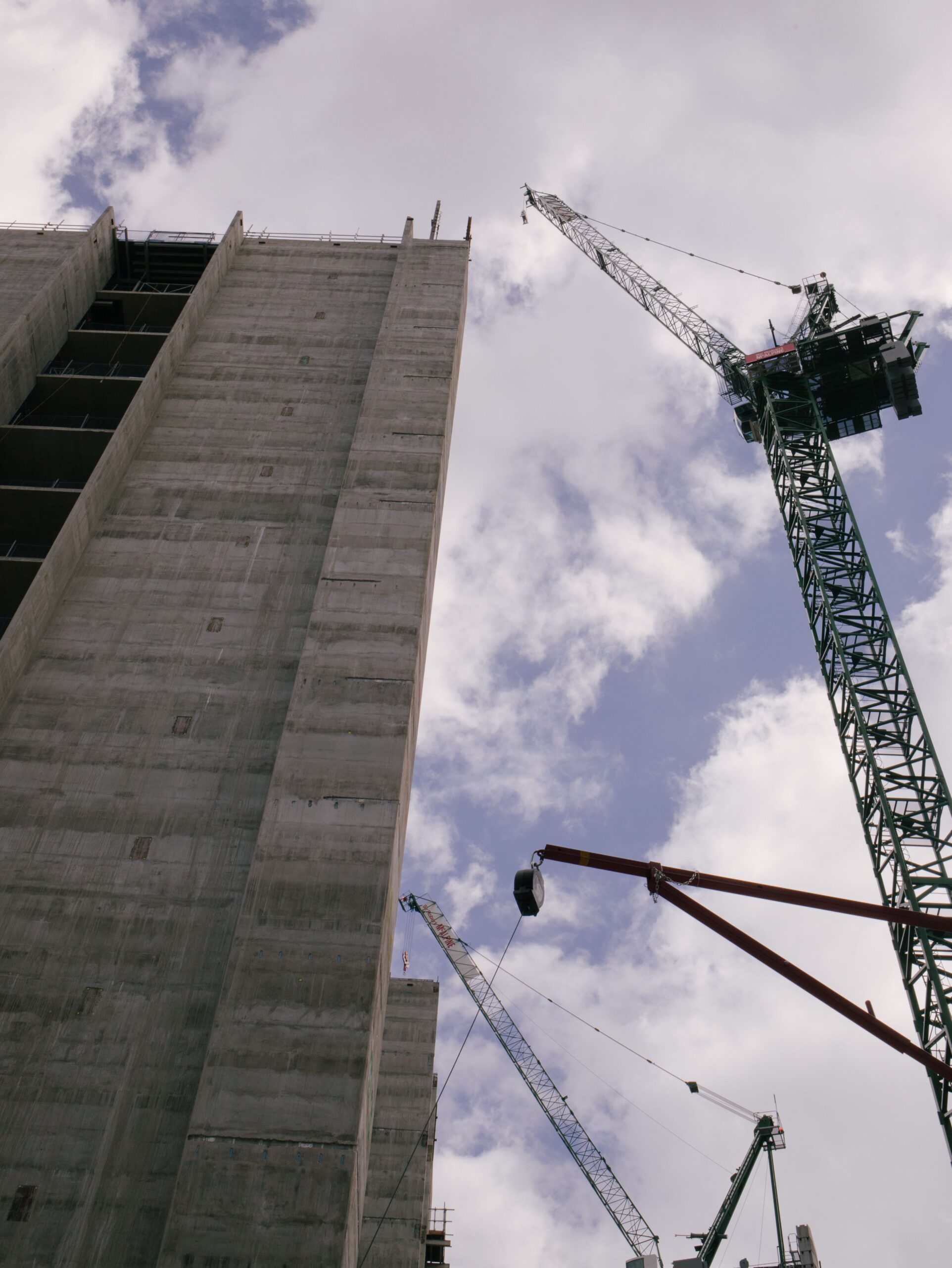 Low angle view of skyscraper under construction with cranes against blue sky.